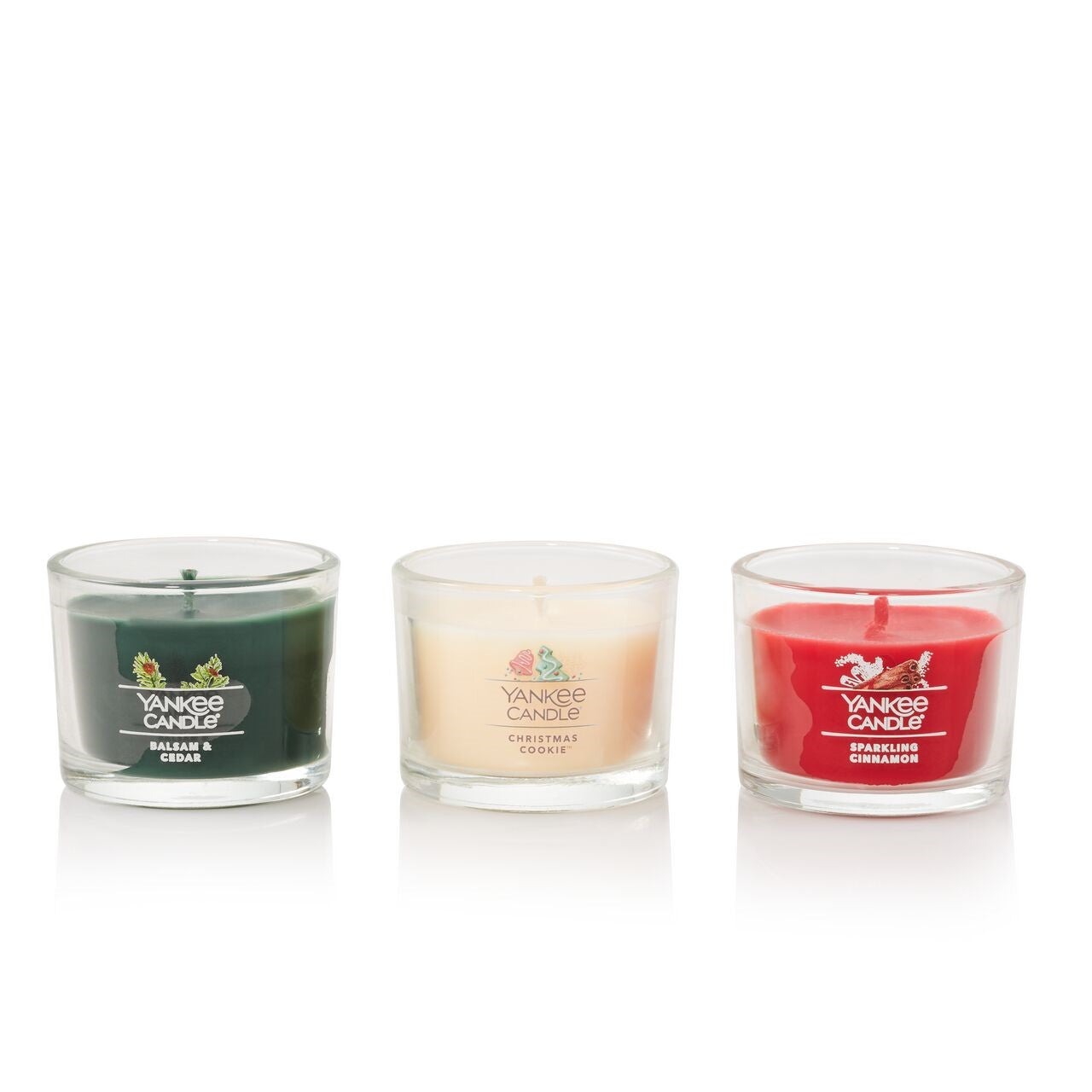 Three scented candles: green, cream, and red. the jars have labels with festive aromas.